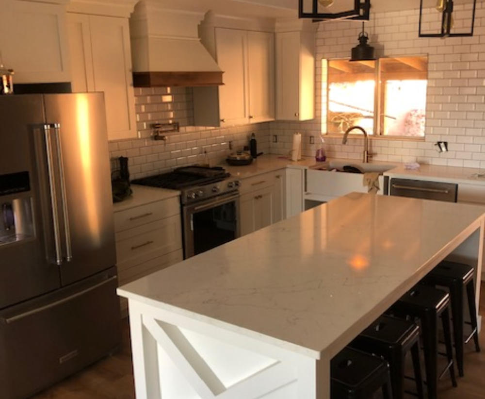A finished Inferno kitchen remodel with a quartz waterfall island, white cabinets, and a subway tile backsplash.