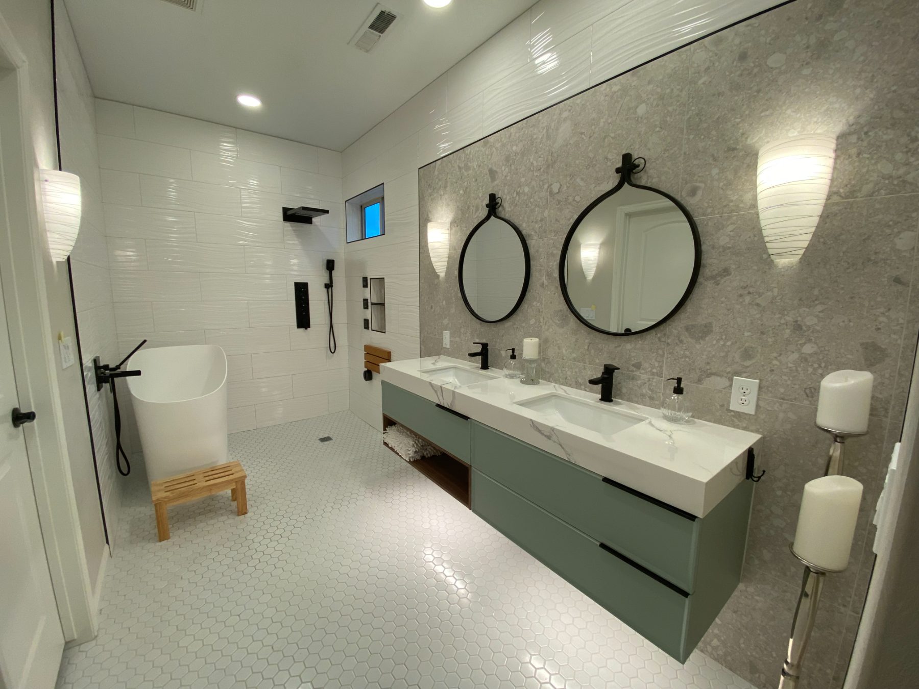 A finished Inferno master bathroom with a sage floating double vanity, quartz counter, freestanding tub, curbless tile shower, and hex mosaic floor.