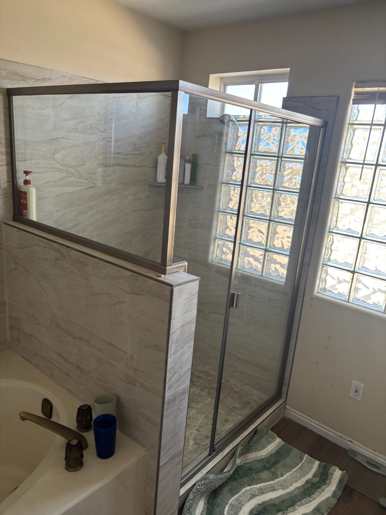 A finished tile shower with a mosaic accent band and glass block window by Inferno Construction.