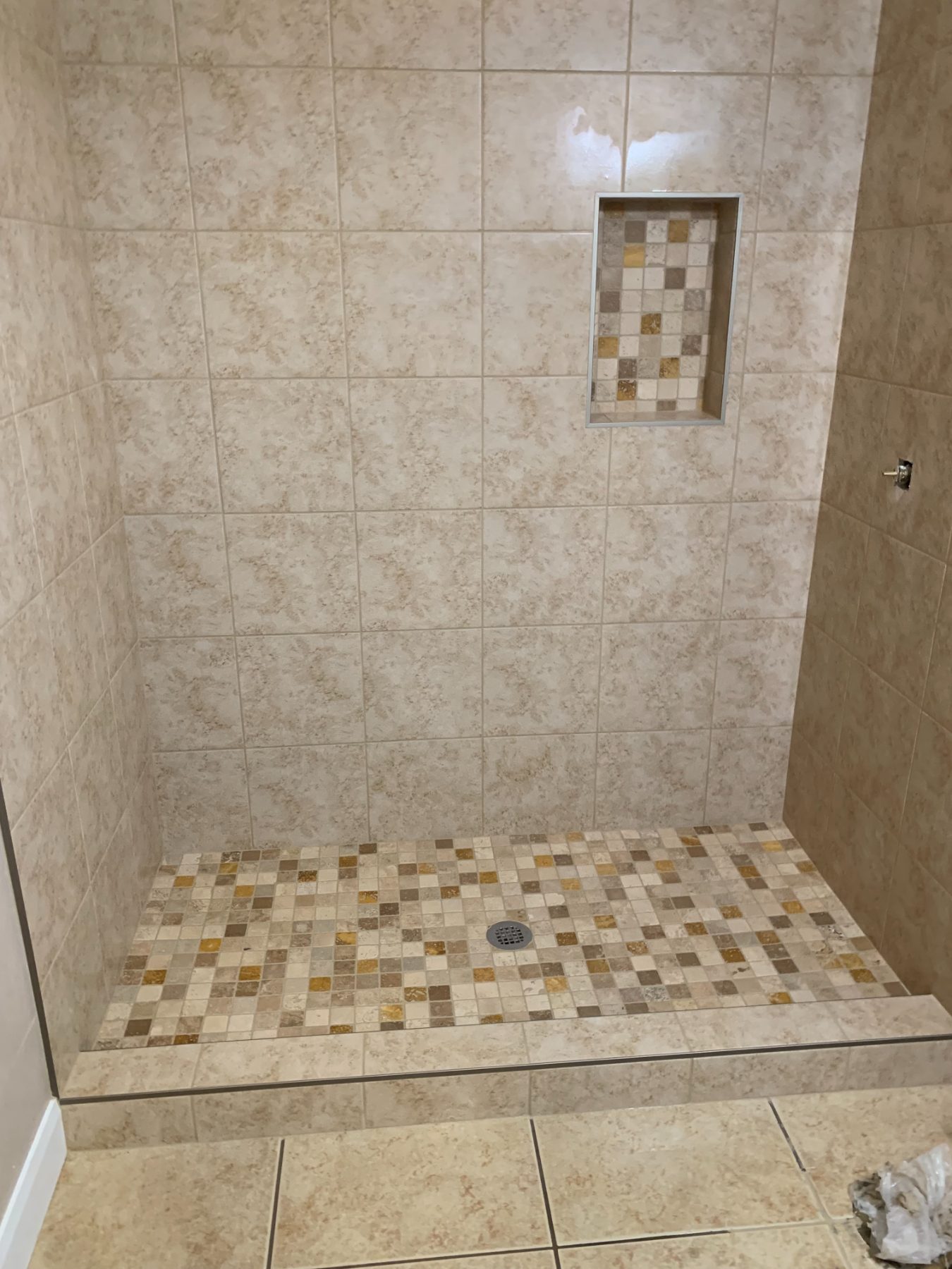 A finished travertine tile shower with a mosaic accent stripe by Inferno Construction.